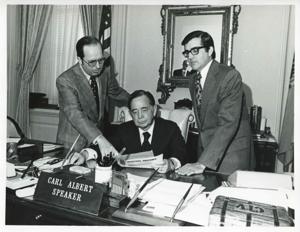 Carl Albert seated at his desk. Two men standing behind him looking at some papers which Albert holds., 1950-01-01 - 1976-12-31