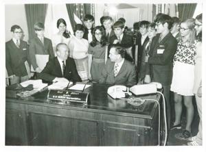 Carl Albert seated at his desk. Behind him is a large group of young people dubbed the quiz-kids., 1950-01-01 - 1976-12-31