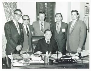 Carl Albert seated at his desk; several men are standing behind him., 1950-01-01 - 1976-12-31