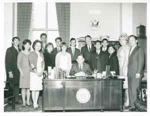 Carl Albert seated at his desk. Behind him is Hale Boggs and a group of high school students from Hawaii., 1950-01-01 - 1976-12-31