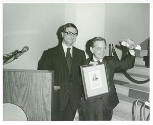 Carl Albert standing next to the podium at his birthday party. He is holding up a plaque., 1950-01-01 - 1976-12-31