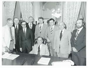 Carl Albert is seated at his desk. Behind him is Thomas E. Morgan and several unidentified men., 1950-01-01 - 1976-12-31