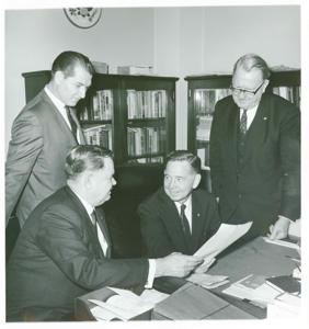 Carl Albert seated next to Carter Bradley. They are looking at documents. Two men are standing behind them., 1950-01-01 - 1976-12-31