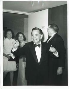 Carl Albert in a hotel room. Mary Albert and another woman are behind him., 1950-01-01 - 1976-12-31