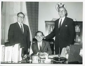 Carl Albert seated at his desk. Two unidentified men are standing behind him., 1950-01-01 - 1976-12-31