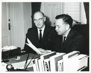 Carl Albert seated at his desk beside an unidentified man. They are looking at documents., 1950-01-01 - 1976-12-31