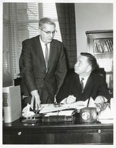 Carl Albert seated at his desk. An unidentified man is standing behind him., 1950-01-01 - 1976-12-31