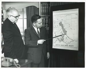 Carl Albert with an unidentified man looking at the Sam Rayburn commemorative stamp., 1950-01-01 - 1976-12-31