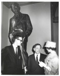 Carl Albert and an unidentified man, shaking hands, under a statue of Will Rogers., 1950-01-01 - 1976-12-31