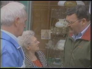 ["In the 1994 presidential campaign ad, Democratic candidate Duke DeTremble confidently speaks at various rallies, promoting strong leadership and community values. Scenes depict him addressing enthusiastic crowds across Maine, bolstered by American and state flags, emphasizing his commitment with a solid, determined demeanor at the podium."]